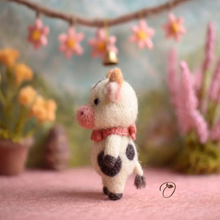 Small cow figurine with a bow tie in a decorative setting with flowers and plants.