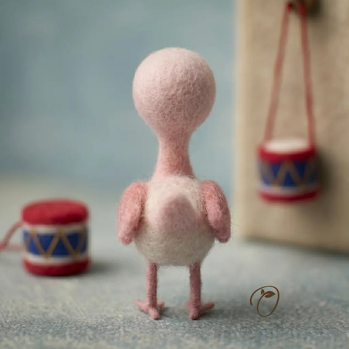 Small pink felt bird toy with a blurred background featuring small drums.
