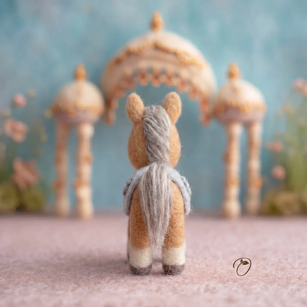 Small stuffed animal with a yarn tail in front of decorative arches and flowers.