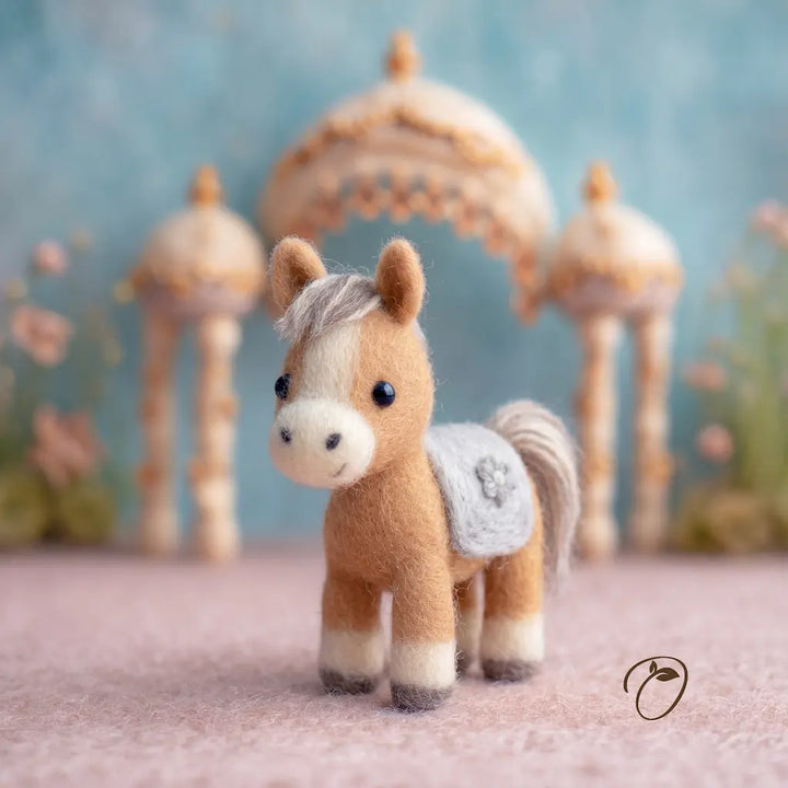 Small brown and white toy horse with a decorative saddle blanket against a soft focus background with lanterns and flowers.