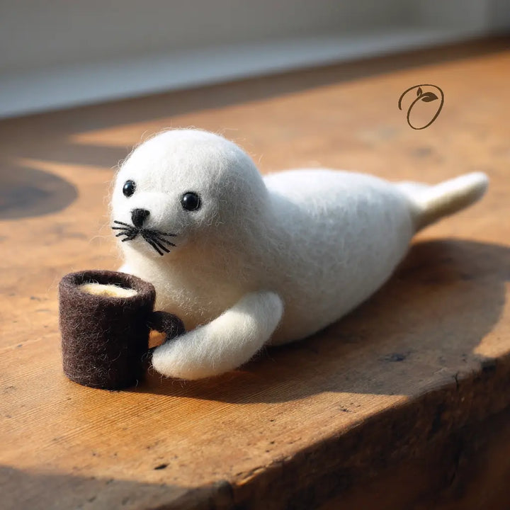 White seal toy holding a brown felt cup on a wooden surface