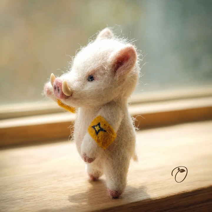 Small felted pig toy with a yellow tag on a wooden surface