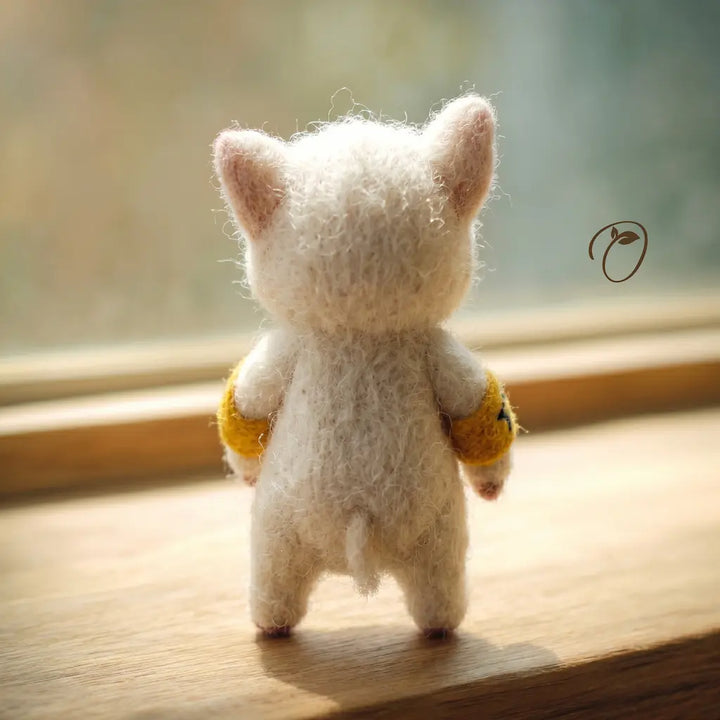 Small felted animal toy, possibly a cat or bear, with yellow accents on a wooden surface.