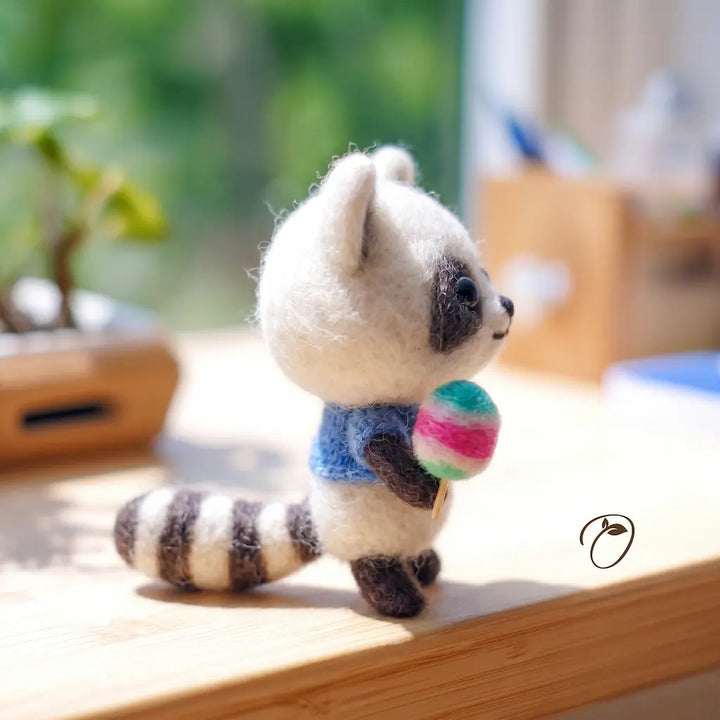 Small plush toy raccoon holding a colorful ball on a wooden surface with a blurred natural background
