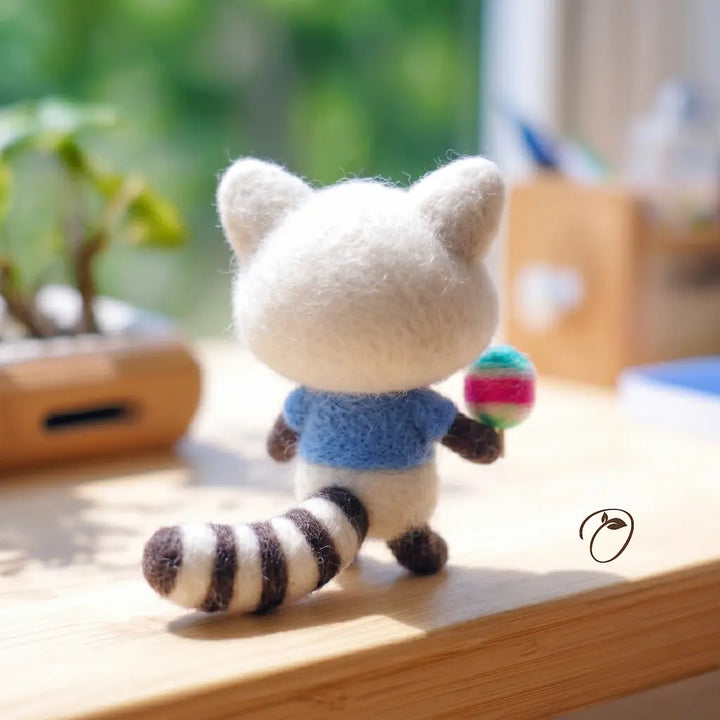 Small plush toy raccoon wearing a blue sweater on a wooden surface with a blurred background