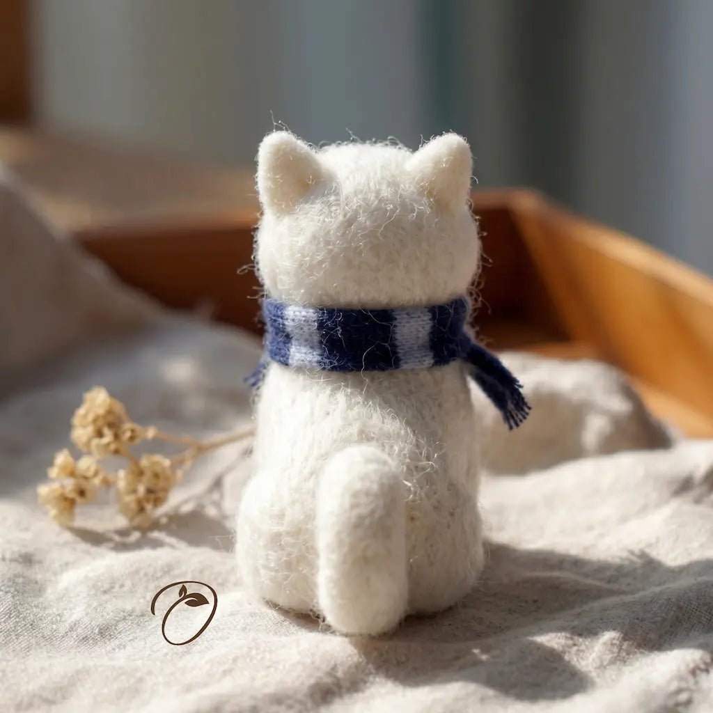 White cat-shaped plush toy wearing a blue scarf on a soft surface with a blurred background