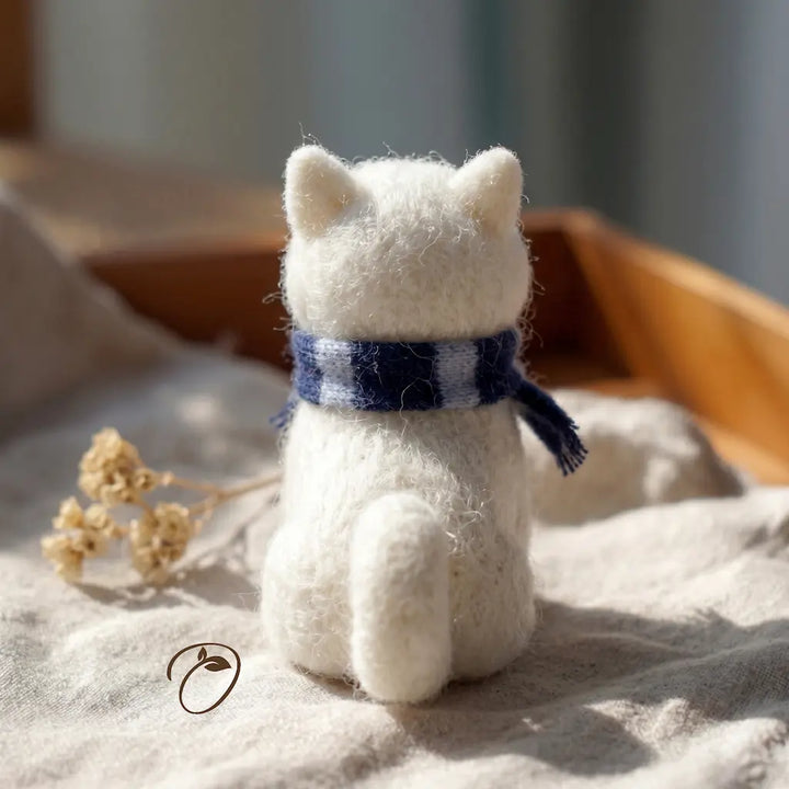 White cat-shaped plush toy wearing a blue scarf on a soft surface with a blurred background