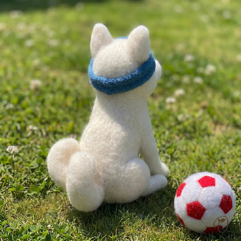 White plush dog toy with a blue bandana sitting on grass next to a red and white ball.