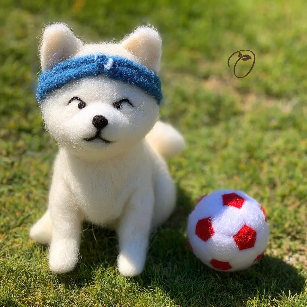White plush dog toy with a blue bandana sitting on grass next to a red and white ball.