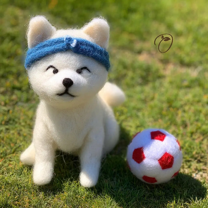 White plush dog toy with a blue bandana sitting on grass next to a red and white ball.