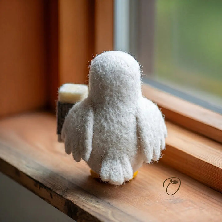 White plush penguin toy on a wooden surface near a window