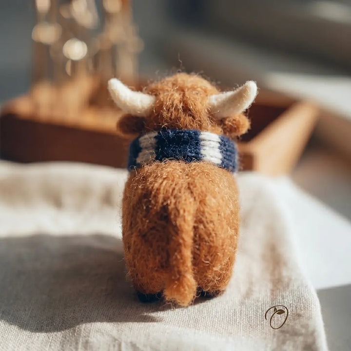 Small brown plush toy with horns and a striped scarf on a light surface.