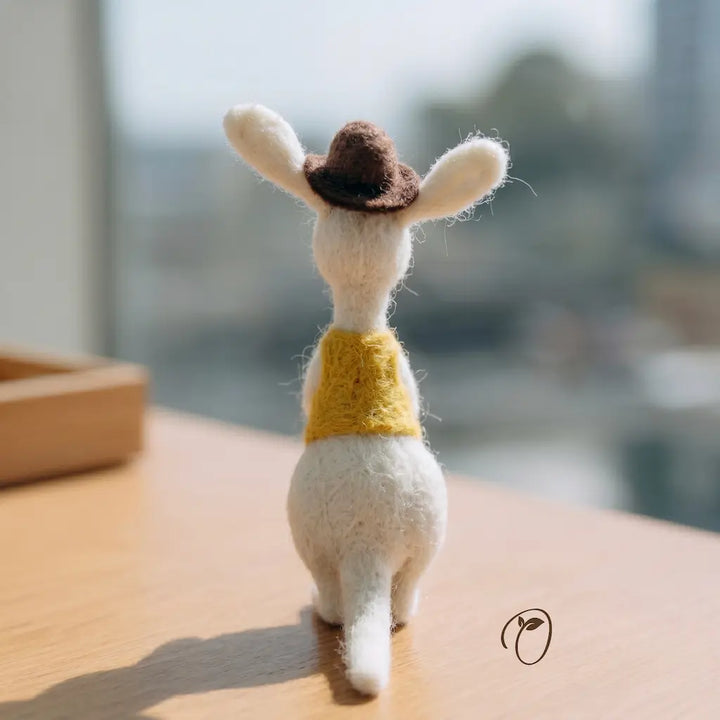 Small felted animal toy with a yellow sweater on a wooden surface