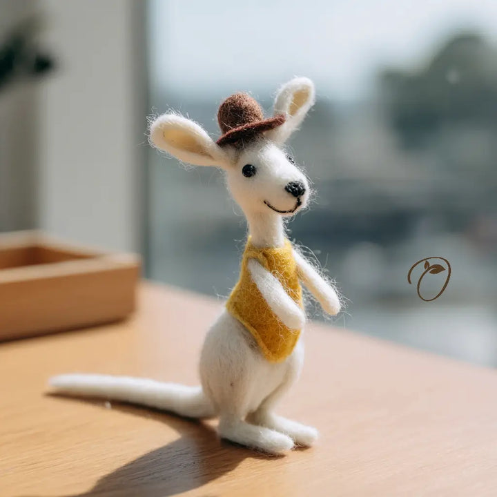 White animal figurine wearing a brown hat and yellow vest on a wooden surface with a blurred natural background.