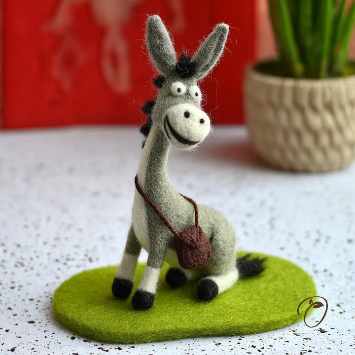 Felt donkey figurine on a green base with a blurred red background