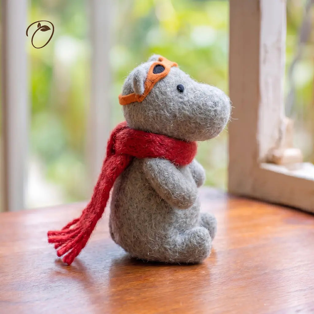 Small gray plush dog with a red scarf and orange goggles on a wooden surface.