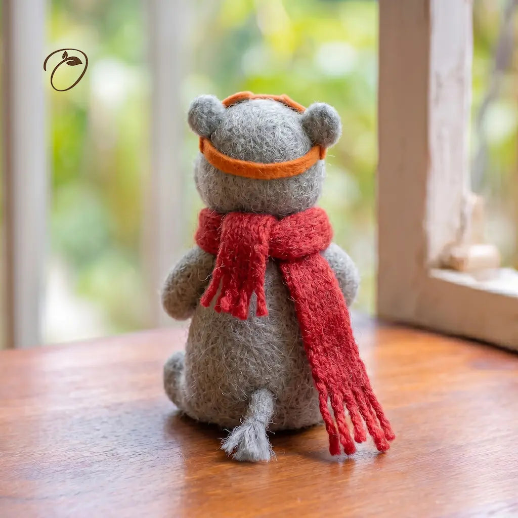 Stuffed animal toy with a red scarf and orange headband on a wooden surface.