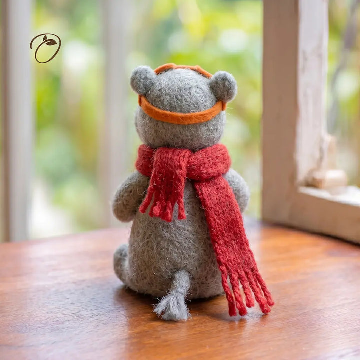 Stuffed animal toy with a red scarf and orange headband on a wooden surface.
