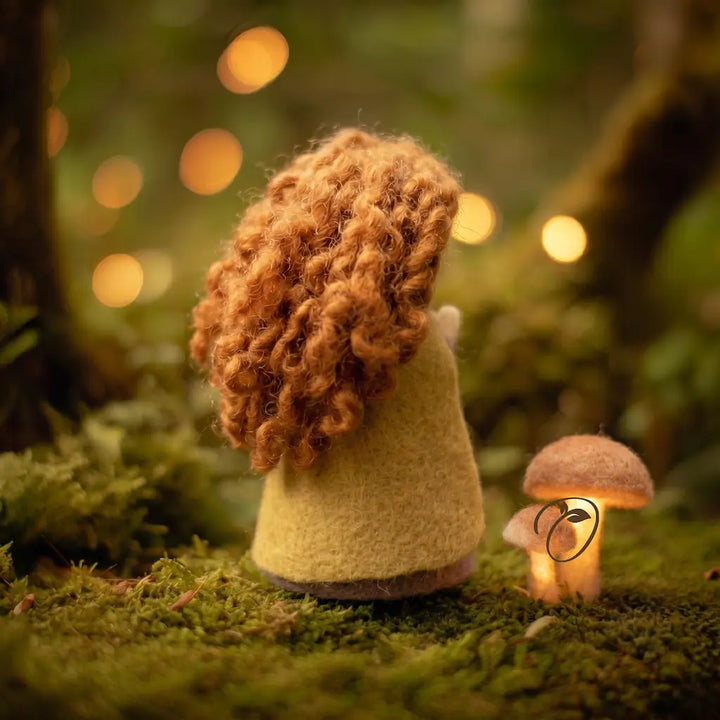 Felted gnome with curly hair standing in a forest with glowing lights and a mushroom.