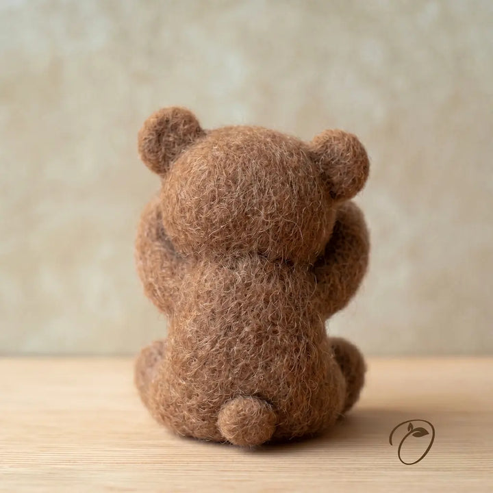 Brown teddy bear plush toy on a wooden surface with a blurred beige background