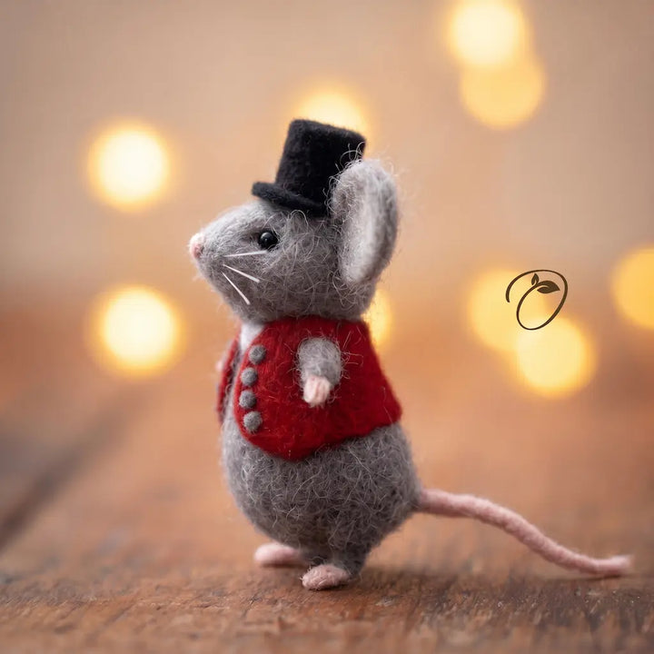 Felted mouse figurine wearing a red jacket and black top hat on a wooden surface with a blurred light background