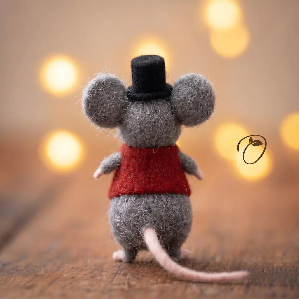 Small mouse figurine wearing a red sweater and black top hat on a wooden surface with blurred lights in the background.
