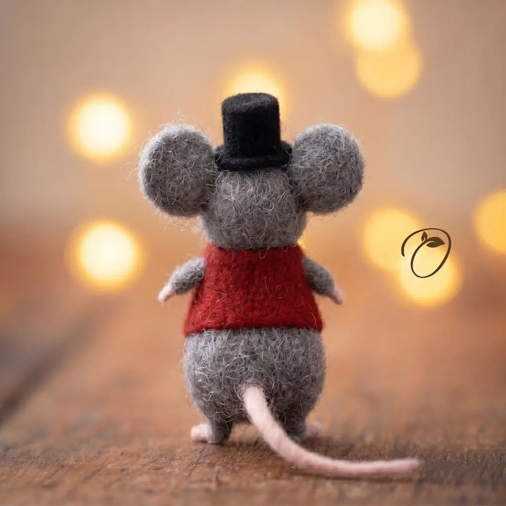 Small mouse figurine wearing a red sweater and black top hat on a wooden surface with blurred lights in the background.