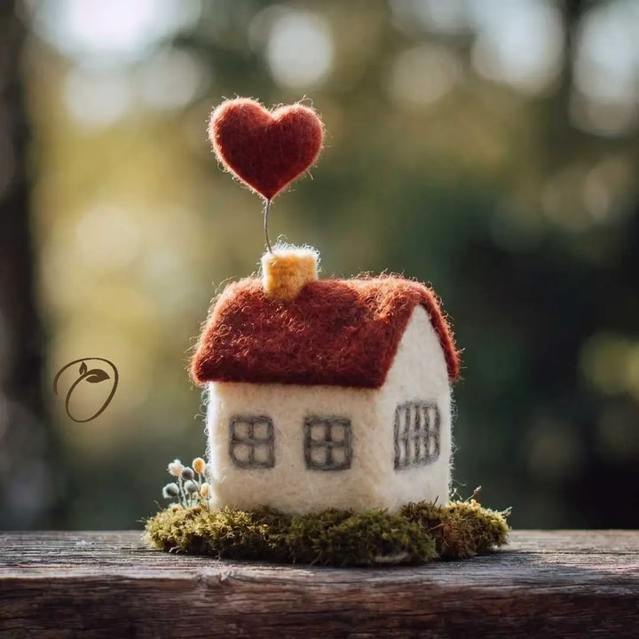 Small felt house with a red heart on top against a blurred natural background
