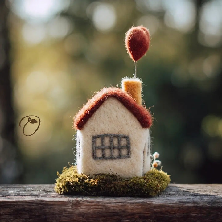 Small felt house with a red roof on a wooden surface with a blurred natural background