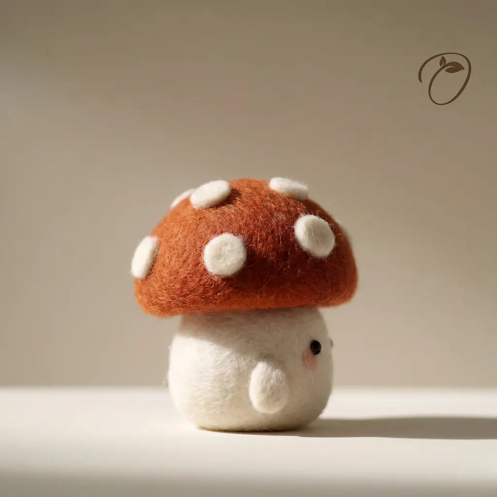 Felted mushroom toy with a red cap and white spots on a neutral background