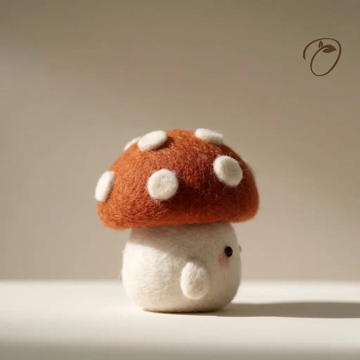 Felted mushroom toy with a red cap and white spots on a neutral background