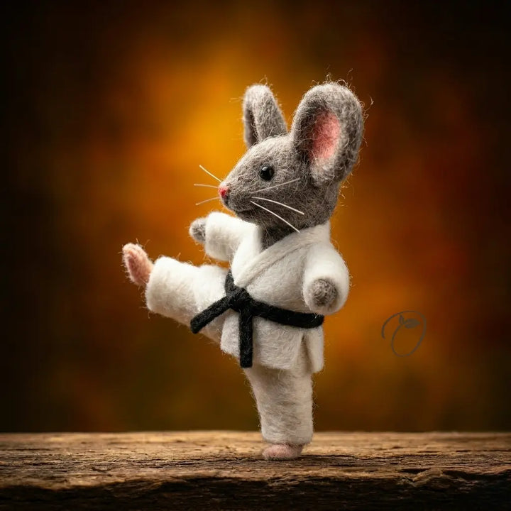 Toy mouse in a karate outfit with a black belt on a wooden surface and dark background