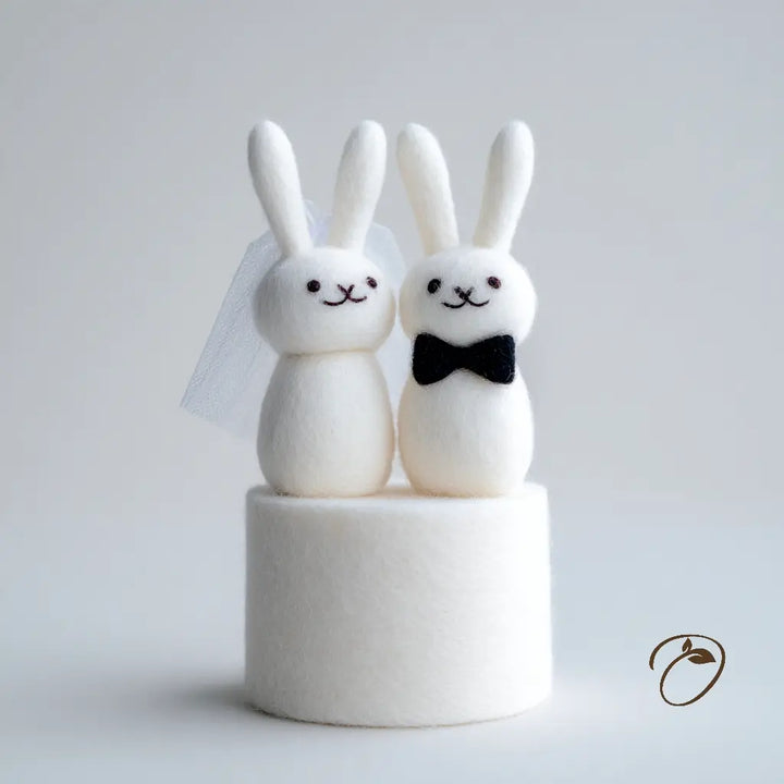 Two white rabbit figurines, one with a bow tie, on a gray background