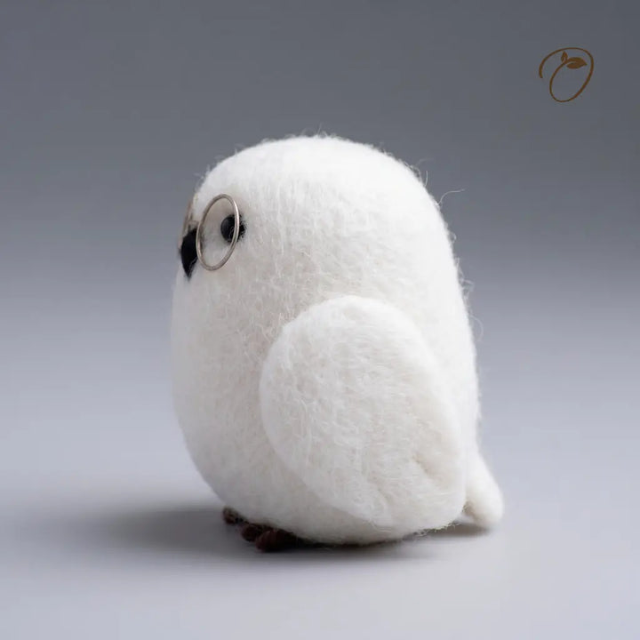 A white felt owl figurine with round wire glasses, a black beak, and small brown feet, photographed against a smooth gray gradient background.