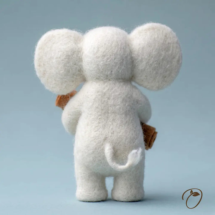 A white felted wool elephant figurine shown from the back, holding a small brown book or package, set against a soft light blue background.
