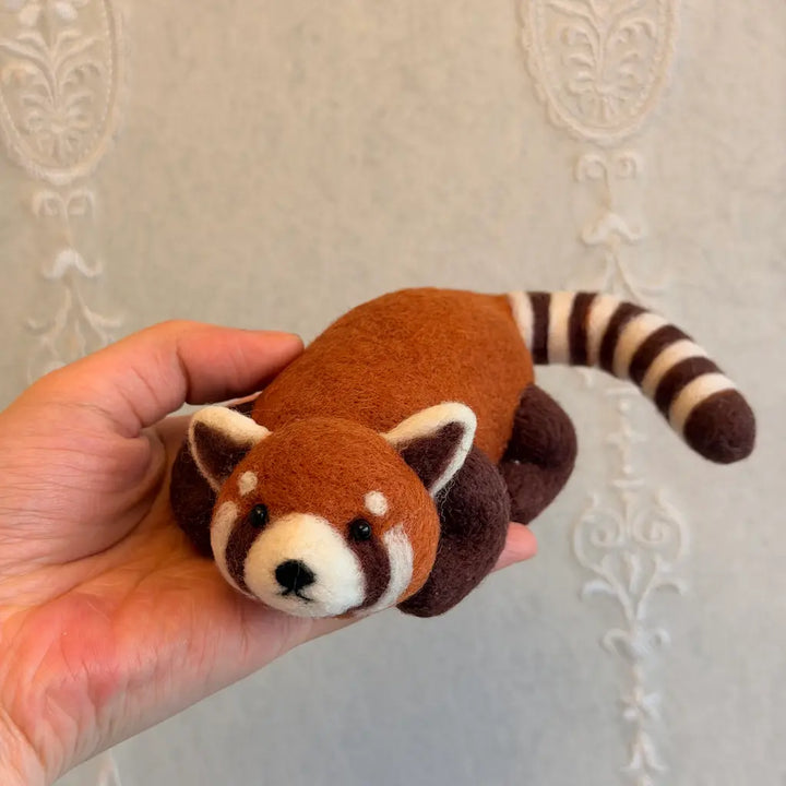 Red panda figurine held in a hand against a neutral background