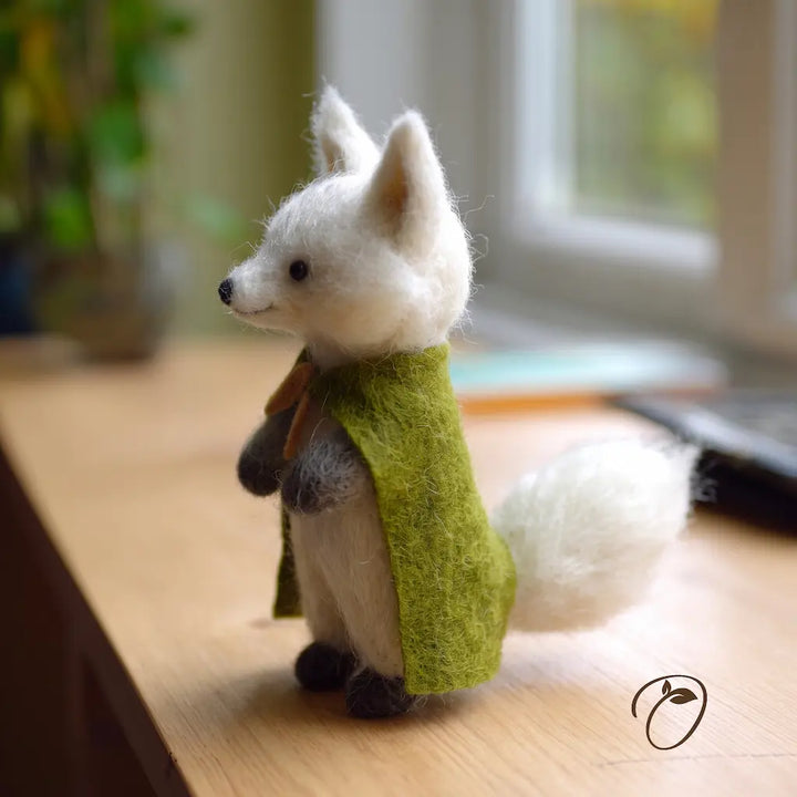 White fox figurine wearing a green sweater on a wooden surface with a blurred background