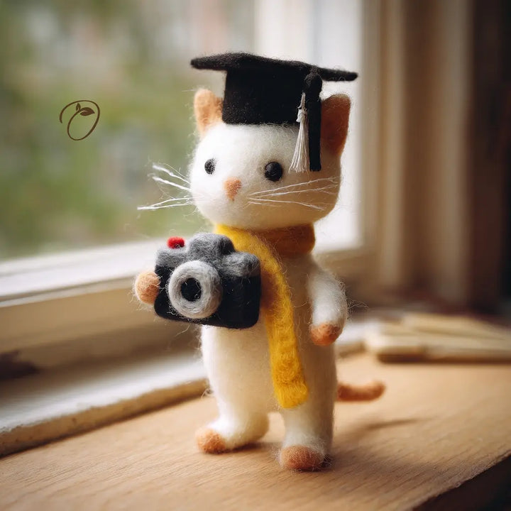 Cat figurine with a graduation cap and camera on a wooden surface