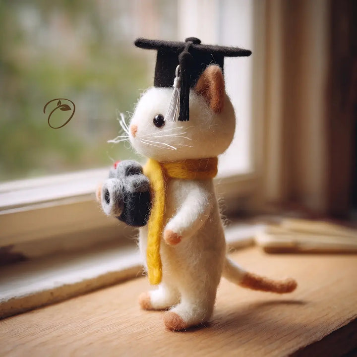 Felted cat with graduation cap and scroll on a wooden surface