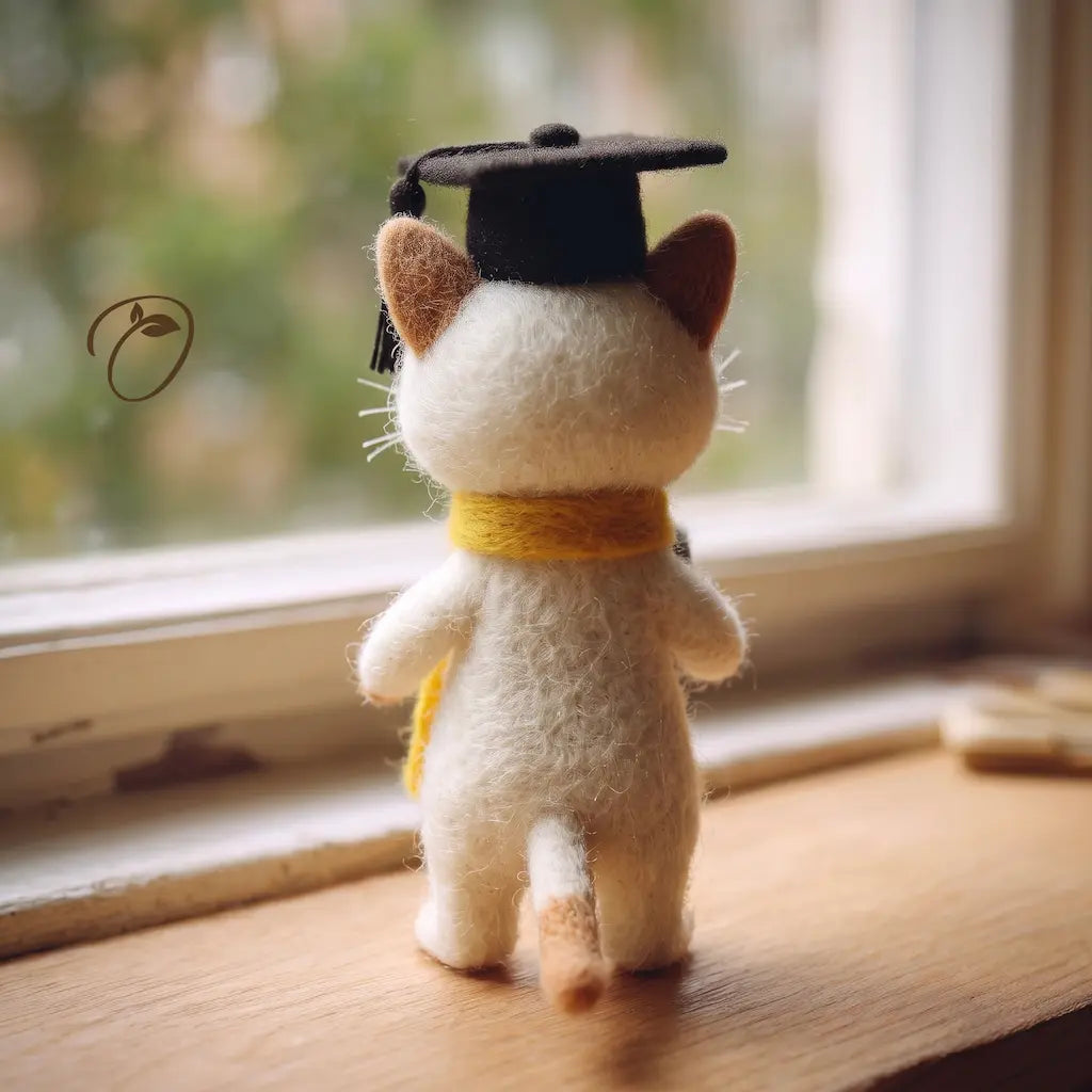 Cat figurine wearing a graduation cap and scarf on a wooden surface with a window in the background