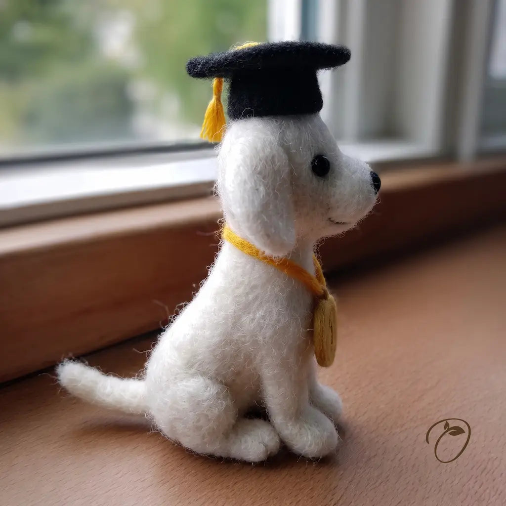 White dog figurine wearing a black graduation cap on a wooden surface with a window in the background.