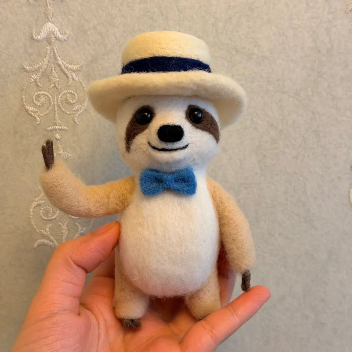 Sloth figurine wearing a hat and bow tie held in a hand against a neutral background