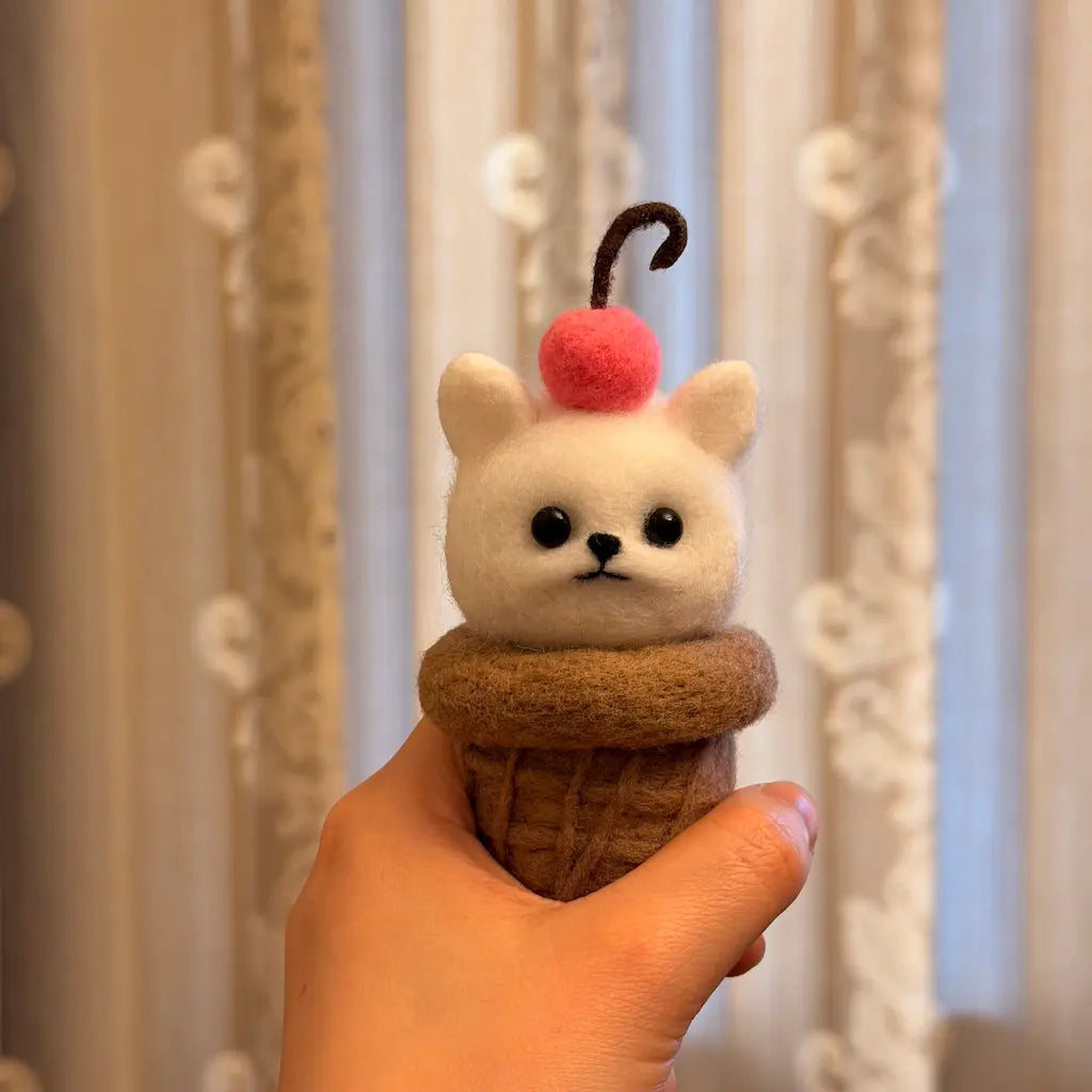 Small figurine resembling a cat in an ice cream cone held by a hand against a curtain background