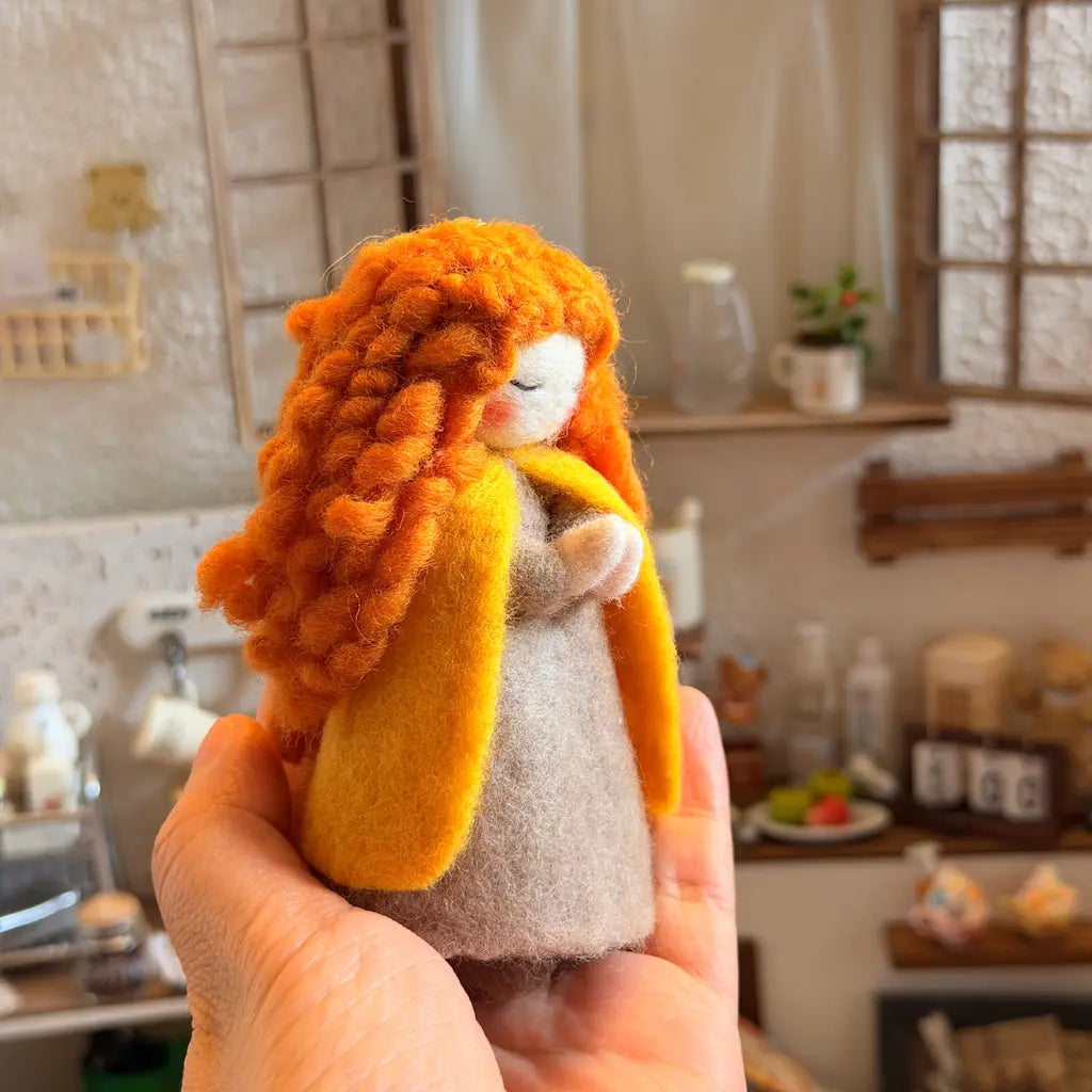 Hand holding a small figurine with orange hair and a yellow scarf in a kitchen setting