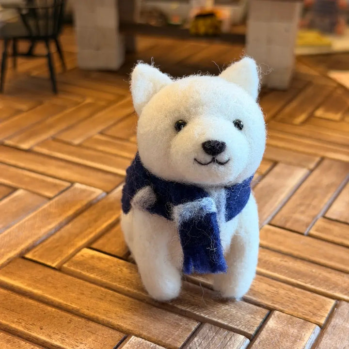 White dog figurine with a blue scarf on a wooden floor
