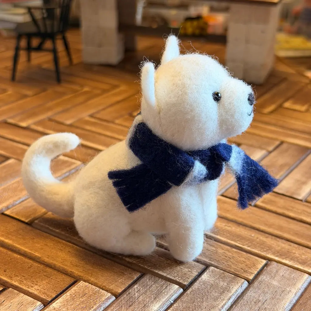 White plush dog figurine with a blue scarf on a wooden floor