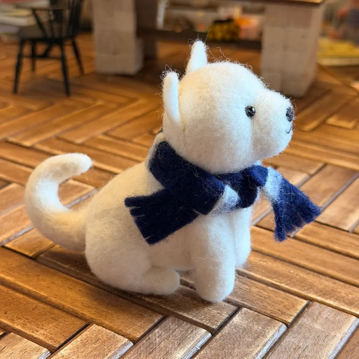 White plush dog figurine with a blue scarf on a wooden floor
