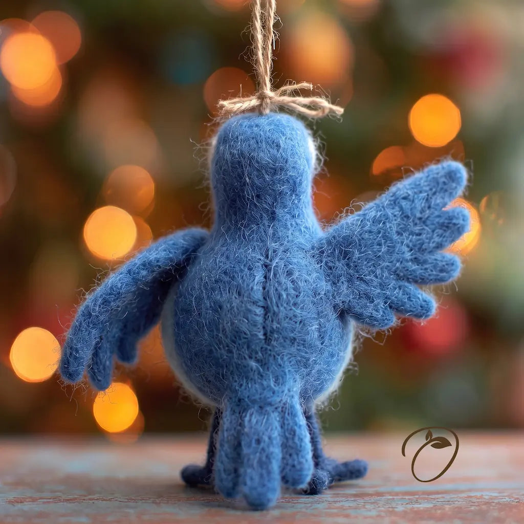 A blue felt bird ornament with wings spread, hanging by a twine loop, photographed on a wooden surface with a blurred festive background of warm lights.