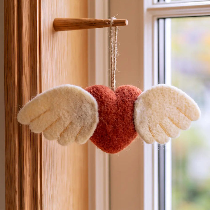 Back of a winged wool felt heart ornament, showing ivory feather shapes, decorative stitching, and a hanging loop.