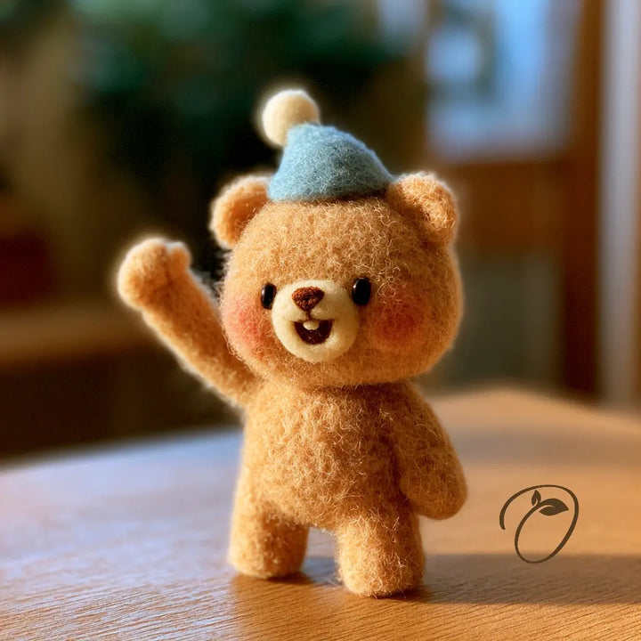 A small felt teddy bear figurine with a light blue hat, standing on a wooden surface with a warm, blurred indoor background.
